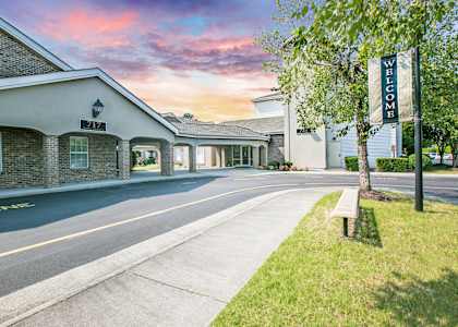 A building with a "Welcome" sign stands next to a tree.