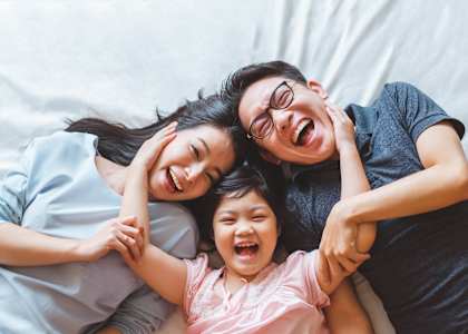 A man and two children are lying down together, smiling and laughing.