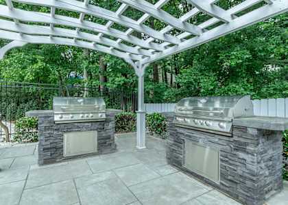 A patio with two stone BBQs under a white pergola at Crest at East Cobb Apartments, Marietta, GA
