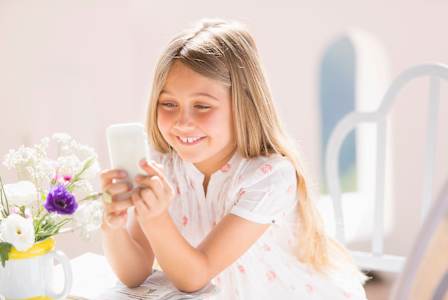 A young girl is smiling while looking at her phone.
