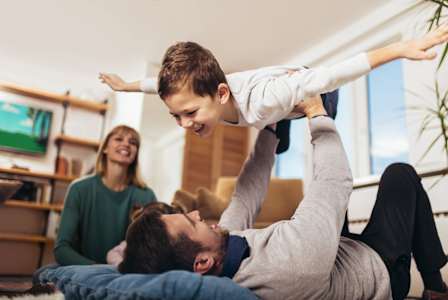 A man is lifting a child in the air while a woman watches.