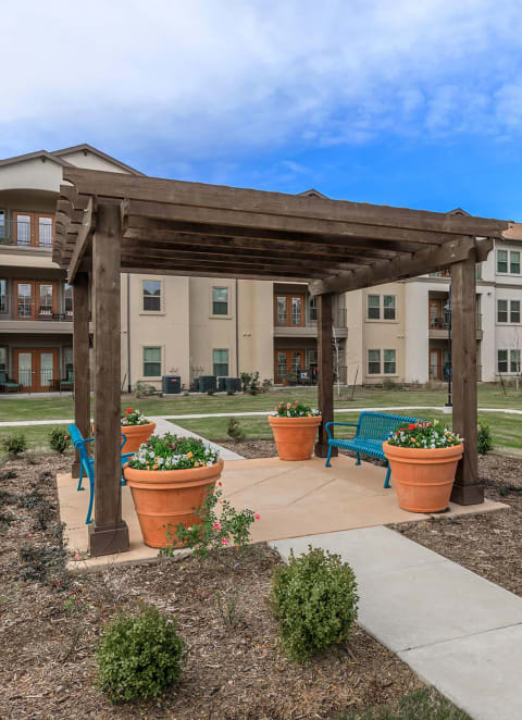 an outdoor area with benches and plants in front of an apartment building at Mariposa at Clear Creek Webster 55+ Apartments, Texas, 77598