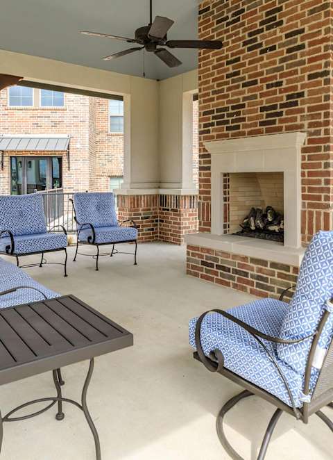a covered patio with blue chairs and a brick fireplace at Mariposa at Westchester, Grand Prairie, TX