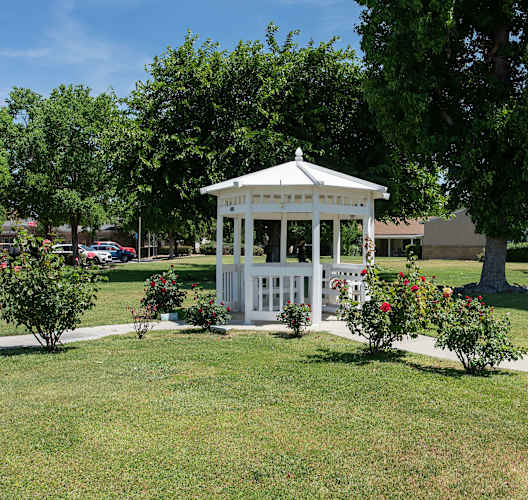 a white gazebo in the middle of a park with trees and flowers at Castle Vista Senior Duplex Community, Atwater, California