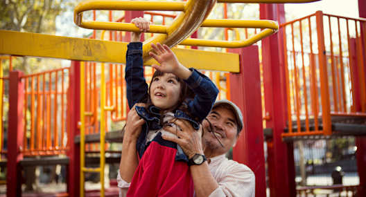 A child is playing on a playground with a man holding them up.