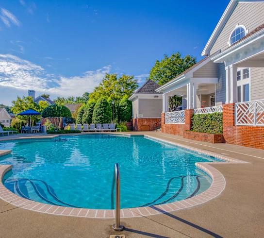 A large outdoor swimming pool surrounded by a brick wall and lounge chairs.