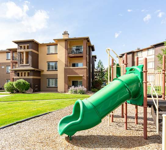a green slide in the middle of a grassy area in front of an apartment complex