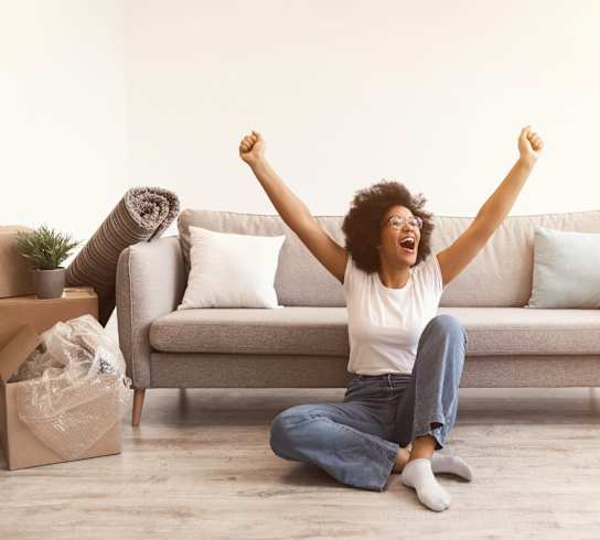 A woman is sitting on the floor with her arms raised in excitement.