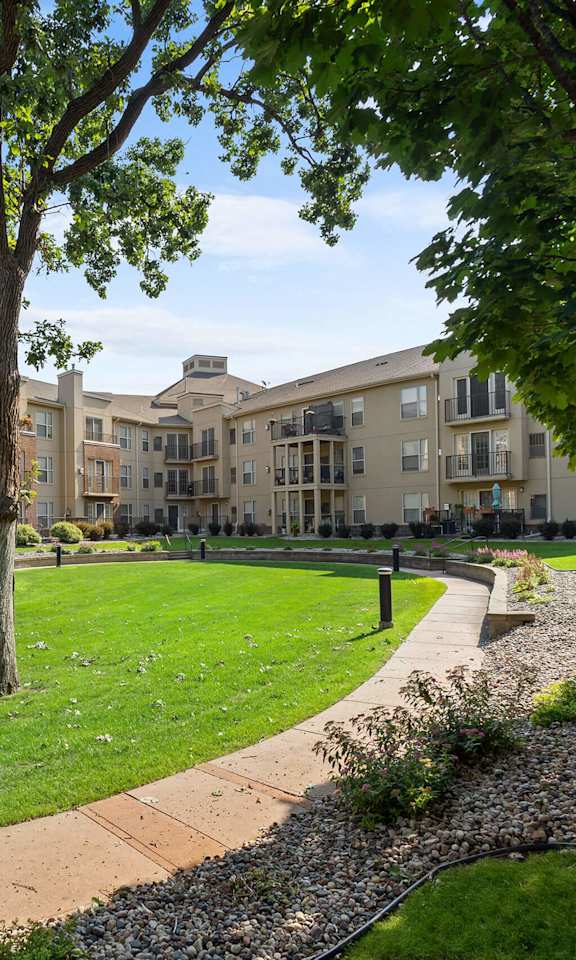 a park with trees and grass in front of an apartment building
