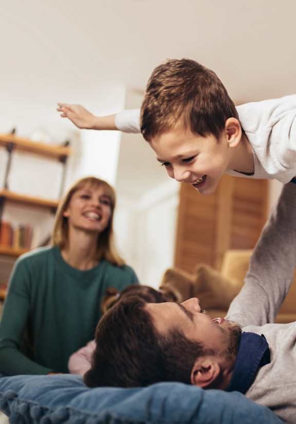 A man is lifting a child in the air while a woman watches.
