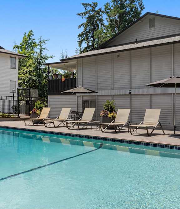 A pool with chairs and umbrellas in front of a house.