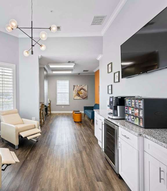 A modern living room with a long white sofa and a grey kitchen area.