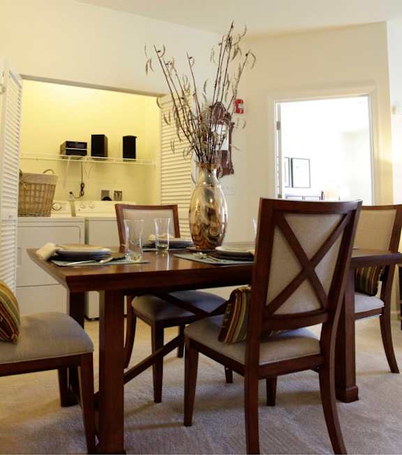 A dining room with a table set for two and a vase of dried flowers on the table.