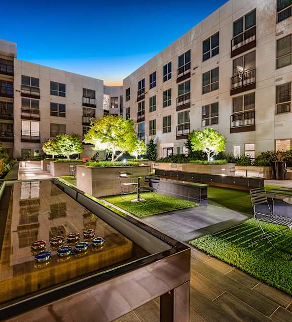 Courtyard game lounge with illuminated shuffleboard table, greenery, and intimate seating under the night sky