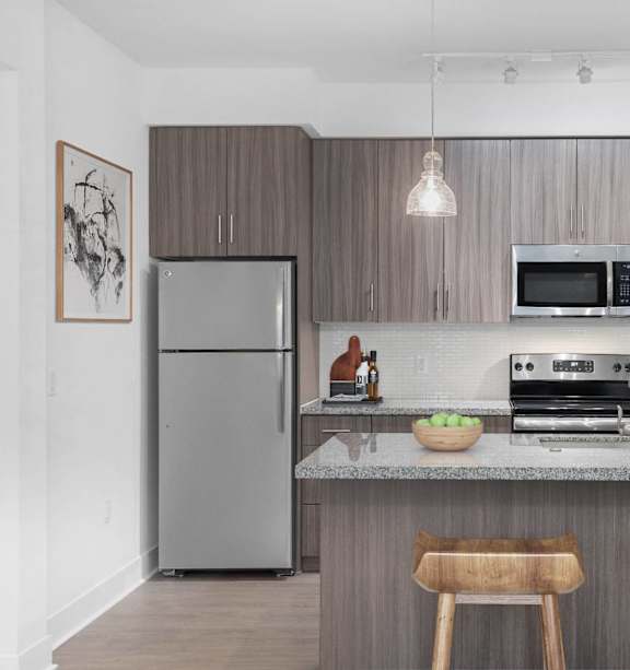 A modern kitchen with a refrigerator, microwave, oven, and a counter with two chairs.