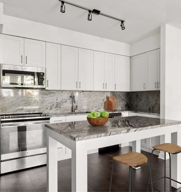 A kitchen with white cabinets and a marble countertop.