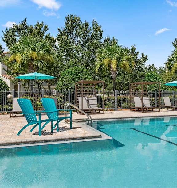 A pool surrounded by trees and chairs.