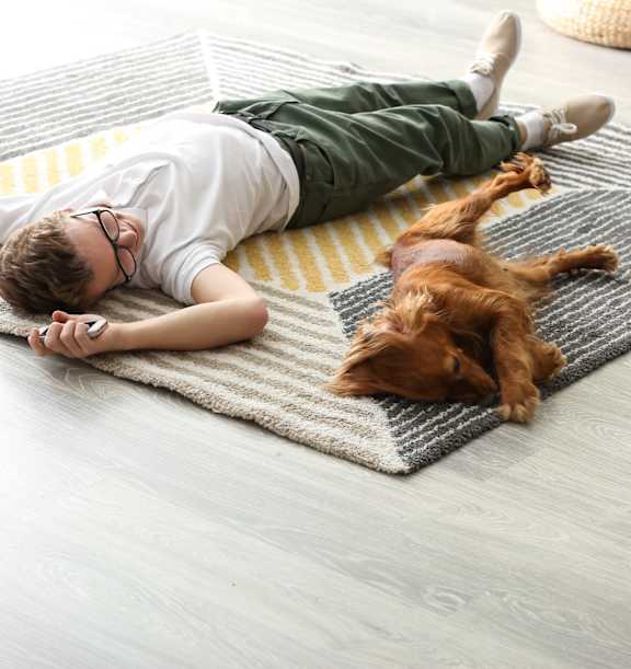 A boy is lying on a rug with his dog.