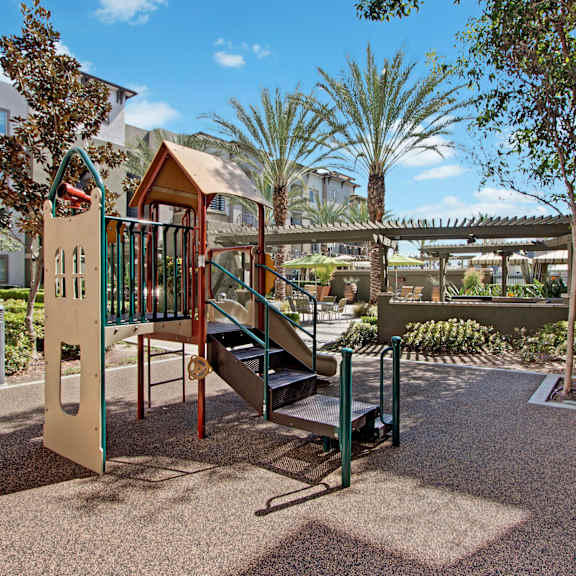 A playground with a slide and stairs in a park and palm trees in the background at Artisan at Main Street Metro.