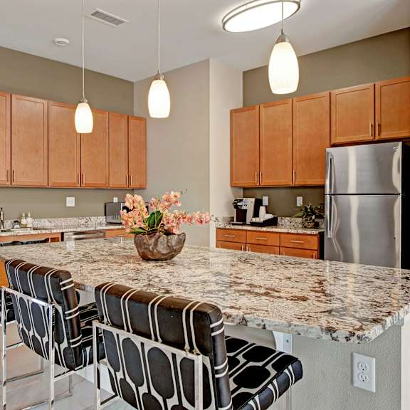 The community kitchen with a coffee machine, toaster, fridge, marble counters, and barstool chairs at Elements at Briargate. 