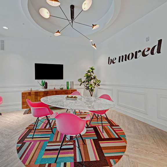 Cyber lounge with bright pink chairs around a table, and a TV mounted on the wall.
