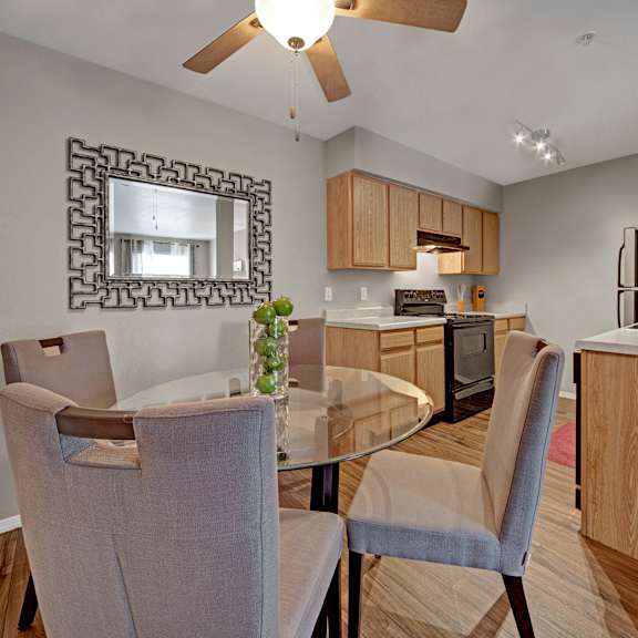 The dining room with a glass dining table and gray chairs and a view of the kitchen with light wooden cabinets and black appliances at Summit Pointe Apartment Homes. 