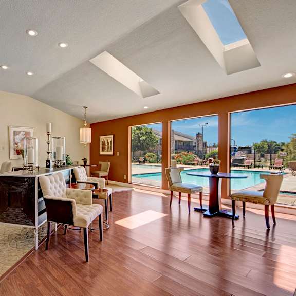 The resident lounge with tables, plush chairs, a couch, and large windows overlooking the window at Cypress Pointe. 