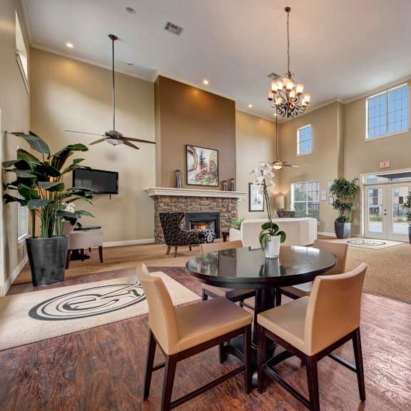 The lounge at Reserve at Abilene with chairs, potted plants, large windows, ceiling fans, a chandelier, coffee tables and a fireplace. 