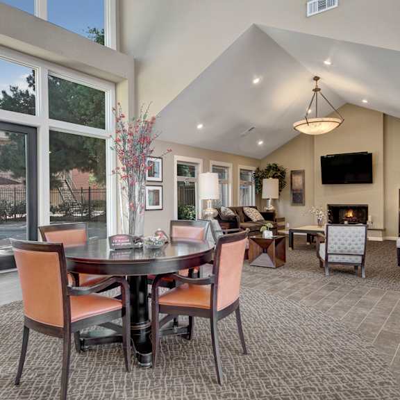 The amazing resident lounge with couches, decorations, large windows, a fireplace, unique overhead lighting, a TV, a dining table and chairs, plush chairs, and coffee tables at the Bradford Apartment Homes. 