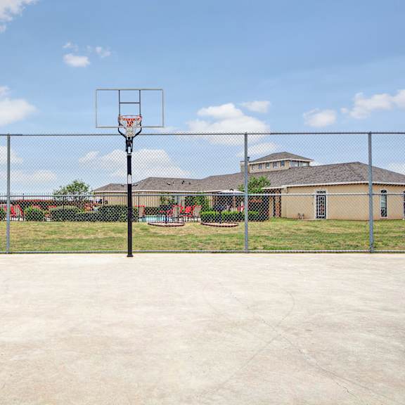 A basketball court for resident use with the pool and the apartment buildings in the background at the Residence at Heritage Park Apartment Homes. 