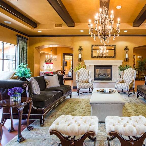 The luxurious resident lounge at Tuscany at Faudree with black velvet couches, a fireplace, coffee tables, a chandelier, wall art, large windows, and plush chairs. 