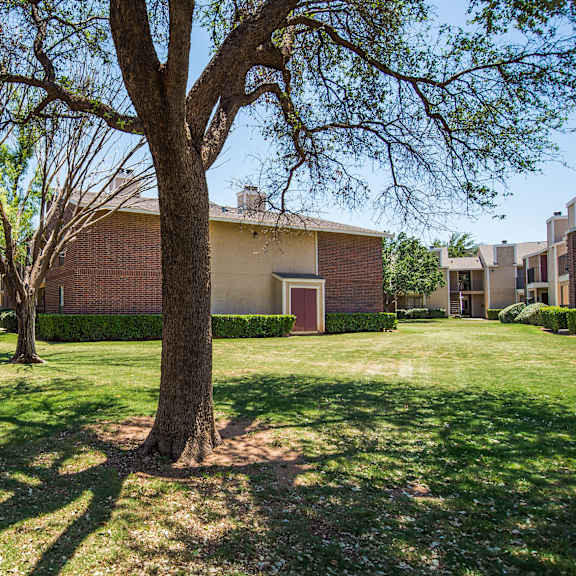 Exterior of the Wildflower apartments, with grass and trees and the red brick apartment buildings in the background. 