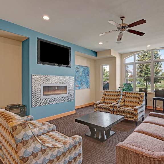 The amazing resident lounge with a fireplace, couches, decorations, a ceiling fan, a blue accent wall, large windows, plush chairs, and coffee tables at Van Buren Place Apartment Homes. 