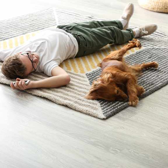 A boy is lying on a rug with his dog.