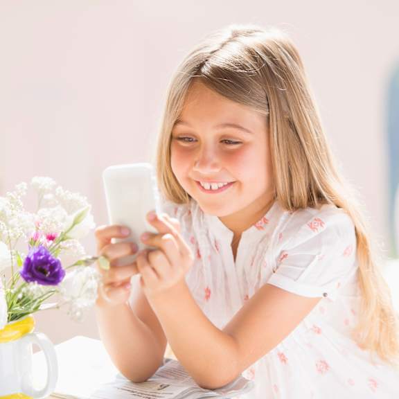 A young girl is smiling while looking at her phone.