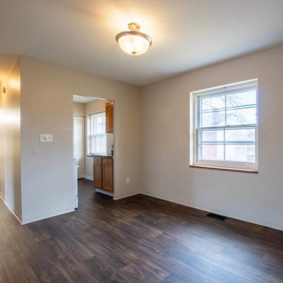 A room with a wooden floor and a kitchenette in the background. at Michigan Street Apartment Homes, Michigan
