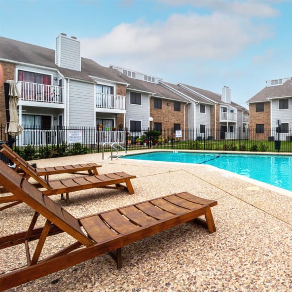 a swimming pool with two wooden benches next to an apartment building at Northchase, Texas, 78753