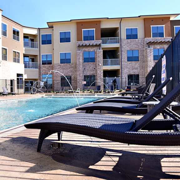 a swimming pool with lounge chairs in front of an apartment building at Urban Square, Denton, 76210