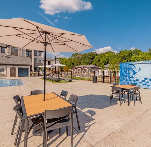 A table with chairs and an umbrella is in the foreground of a patio area.at Evolve at Parkway Apartment Homes, North Carolina