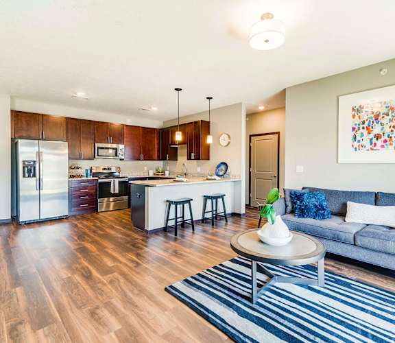 A modern kitchen with dark wooden cabinets, stainless steel appliances, and a peninsula counter that opens to a living room.