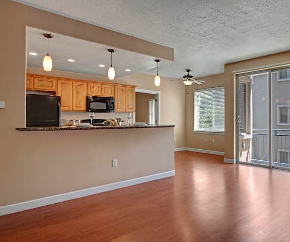 An empty living room with hardwood flooring and kitchen with a door to a balcony at Bridges Apartment Homes. 