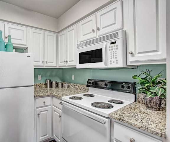 A cozy kitchen with white appliances, light counter, and spacious wooden cabinets at Legends at River Oaks Apartment Homes. 