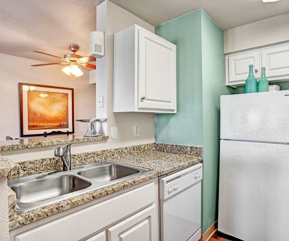 A cozy kitchen with white appliances, light marble counter, and spacious white wooden cabinets at Legends at River Oaks Apartment Homes. 