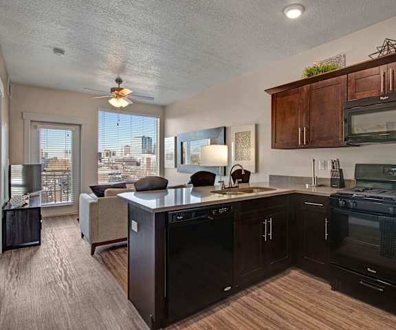 A spacious kitchen with black appliances, dark granite countertops with lots of room, and dark wooden cabinets with decorations at Velo on the Boulevard Apartment Homes. 