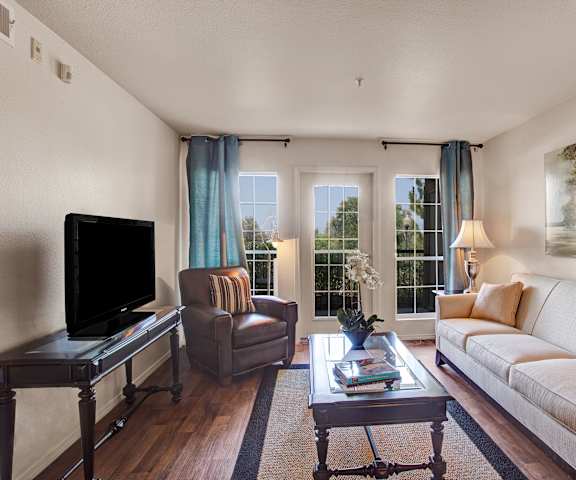 The living room with a couch, plush chairs, coffee table, decorations, a TV, and balcony at Legends at River Oaks Apartment Homes. 