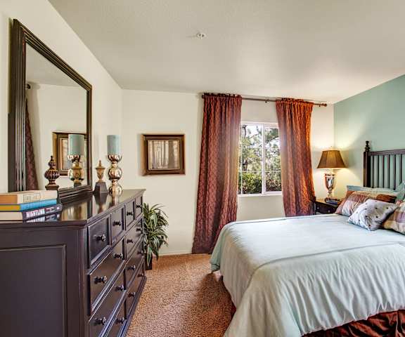 A bedroom with a queen-size bed, a dresser, decorations, window, and nightstands at Legends at River Oaks Apartment Homes. 