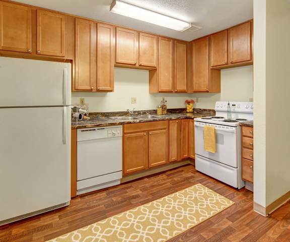 A kitchen with white appliances and marble counters at Conifer Grove Apartments. 