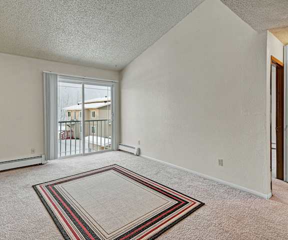 An empty living room with carpeting and a door to the balcony at Confier Grove. 