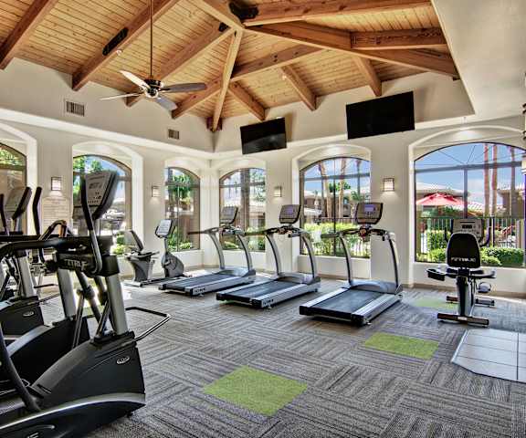 A gym with cardio machines, windows, TVs, and weights at Reserve at Arrowhead Apartment Homes. 
