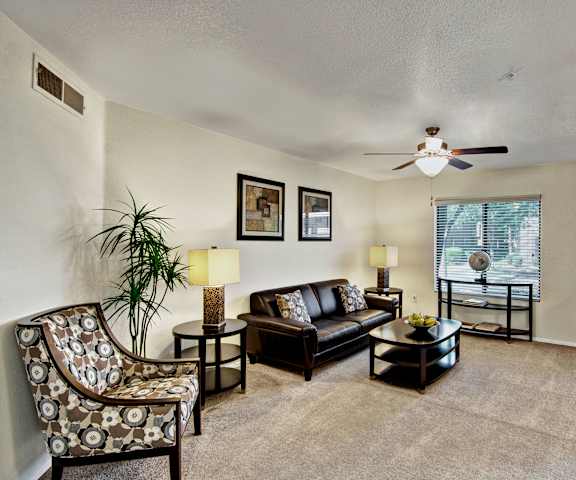 The living room with a couch, ceiling fan and overhead lighting, plush chairs, coffee table, decorations, a TV, and window at Reserve at Arrowhead Apartment Homes. 